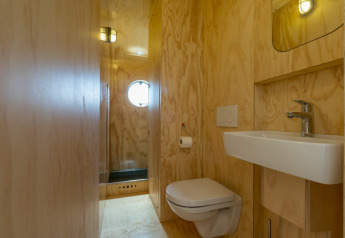 Badkamer met houten wanden, wandtoilet, wastafel en rond raam in een Wikkelhouse in Zeeland, Nederland.