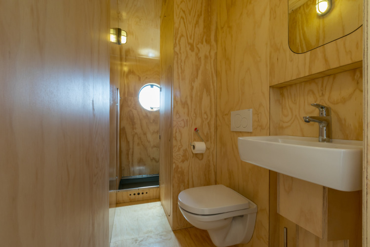 Baño con paredes de madera, inodoro suspendido, lavabo y ventana redonda en un Wikkelhouse en Zelanda, Países Bajos.