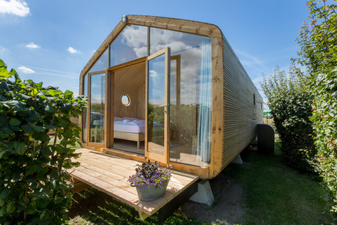 Wikkelhouse met grote glazen gevel en houten veranda, omringd door groen bij Welcome In - Zeeland.