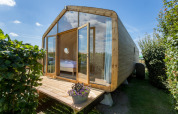Wikkelhouse with large glass facade and wooden porch, surrounded by greenery at Welcome In - Zeeland.