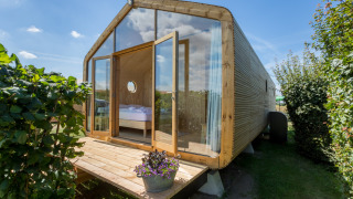 Wikkelhouse met glazen voorgevel en houten terras, omringd door groen, bij Welcome In - Zeeland.