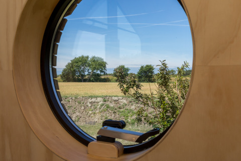 Vista a través de una ventana redonda en una Wikkelhouse en Welcome In - Zeeland, Países Bajos, con campos.