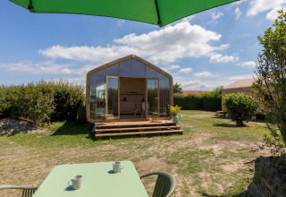 Vista de una Wikkelhouse en Welcome In - Zeeland, Países Bajos, con terraza, mesa y sombrilla verde.