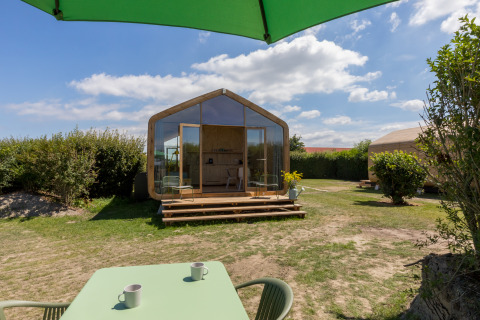 Vista de una Wikkelhouse en Welcome In - Zeeland, Países Bajos, con terraza, mesa y sombrilla verde.