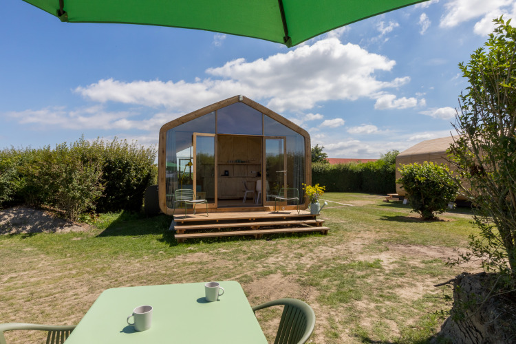 Vista de una Wikkelhouse en Welcome In - Zeeland, Países Bajos, con terraza, mesa y sombrilla verde.