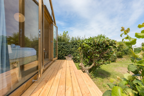 Terraza de madera de una Wikkelhouse en Welcome In - Zeeland, Países Bajos, con vistas a jardín y cielo azul.