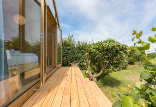 Terraza de madera de una Wikkelhouse en Welcome In - Zeeland, Países Bajos, con vistas a jardín y cielo azul.