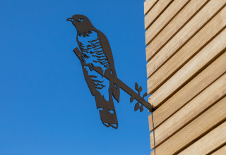 Metalen vogel op de gevel van een Wikkelhouse bij Welcome In - Zeeland, Nederland, tegen blauwe lucht.
