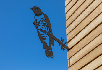 Metallvogel-Silhouette an der Außenwand eines Wikkelhouse in den Niederlanden vor blauem Himmel.