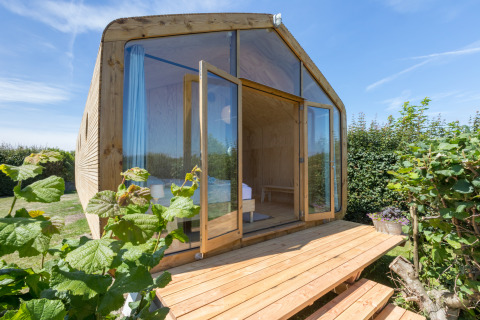 Wikkelhouse met houten gevel en grote glazen deuren, omgeven door groen in Zeeland, Nederland.