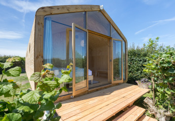 Wikkelhouse con esterno in legno e grandi porte in vetro, immersa nel verde a Zeeland, Paesi Bassi.