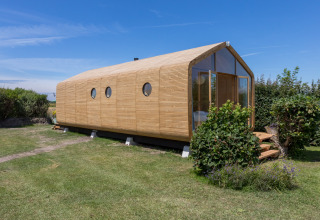 Wikkelhouse en Welcome In - Zeeland, Países Bajos, casa moderna y sostenible de madera rodeada de césped.