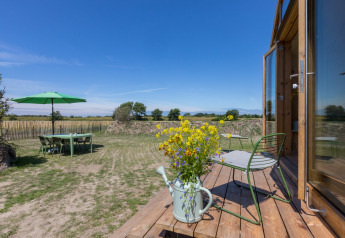 Vista desde un Wikkelhouse en Zeeland, Países Bajos, con terraza, silla verde, flores y mesa de jardín.