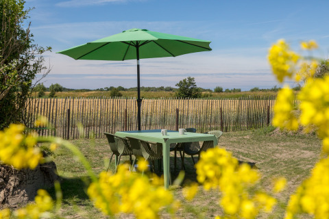 Zona de comedor exterior con mesa, sillas y sombrilla verde en Wikkelhouse en Zeeland, Países Bajos, en verano.