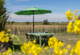Zona de comedor exterior con mesa, sillas y sombrilla verde en Wikkelhouse en Zeeland, Países Bajos, en verano.