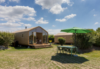 Dos modernas cabañas Wikkelhouse y una mesa al aire libre con sombrilla verde en Welcome In - Zeeland, Países Bajos.