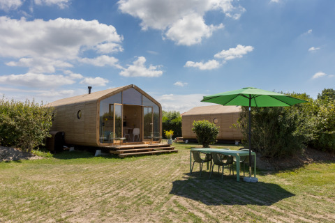 Dos modernas cabañas Wikkelhouse y una mesa al aire libre con sombrilla verde en Welcome In - Zeeland, Países Bajos.