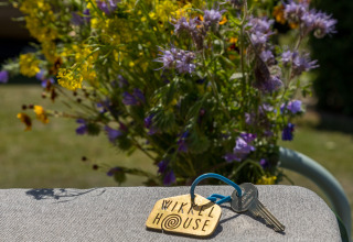 Llaves con etiqueta 'Wikkelhouse' sobre una silla, flores silvestres detrás, Welcome In - Zeeland, Países Bajos.