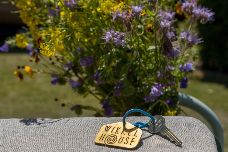Llaves con etiqueta 'Wikkelhouse' sobre una silla, flores silvestres detrás, Welcome In - Zeeland, Países Bajos.