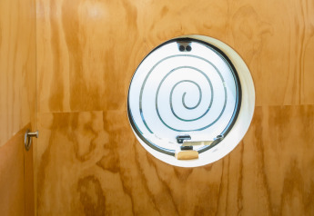 Finestra rotonda con design a spirale in una parete di legno, fotografata in un Wikkelhouse a Zeeland, Paesi Bassi.