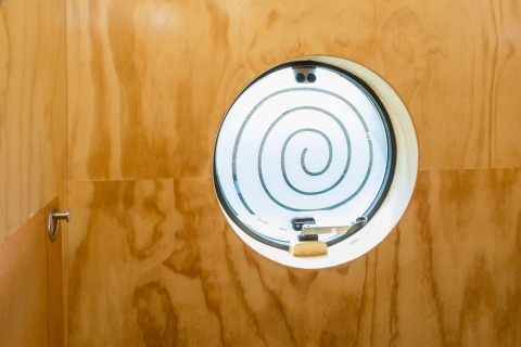 Rundes Fenster mit Spiralmuster in einer Holzwand, gesehen im Inneren eines Wikkelhouse in Zeeland, Niederlande.