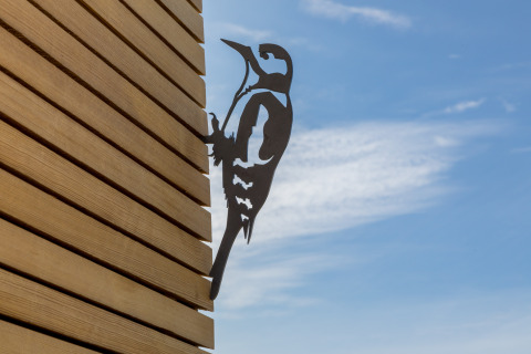 Metallsilhouette eines Spechts an einer Holzwand bei Wikkelhouse im Welcome In - Zeeland, Niederlande.