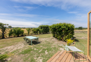 Außenbereich eines Wikkelhouse bei Welcome In - Zeeland, mit Tisch, Stühlen und Blick auf Felder.