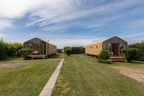 Twee houten Wikkelhouses op grasveld bij Welcome In - Zeeland, Nederland, met blauwe lucht en groen.