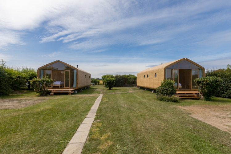 Dos Wikkelhouses de madera en césped en Welcome In - Zeeland, Países Bajos, bajo cielo azul y vegetación.