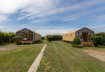 Twee houten Wikkelhouses op grasveld bij Welcome In - Zeeland, Nederland, met blauwe lucht en groen.
