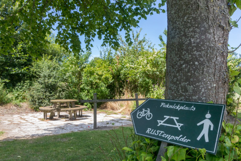 Área de picnic junto a una Wikkelhouse en Zeeland, Países Bajos, con bancos, mesa y letrero bajo árboles.