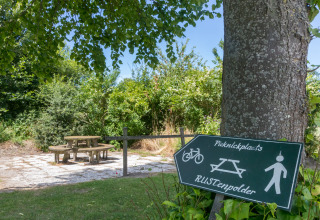 Picknickplatz am Wikkelhouse in Zeeland, Niederlande, mit Tisch, Bänken und Schild im grünen Schatten.