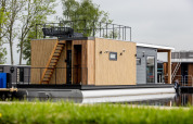 Moderne husbåd ved vandet med træbeklædning, tagterrasse og udendørs trappe i Friesland, Holland.