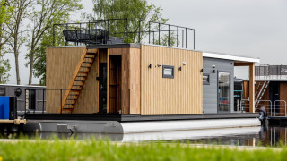 Moderne woonboot met houten gevelbekleding, dakterras en steiger aan het water in Friesland, Nederland.
