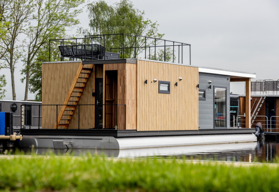Moderne Hausboot mit Holzverkleidung und Dachterrasse, vertäut am Wasser in Friesland, Niederlande.