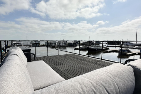 Vista desde una terraza en el Houseboat 'Riggelbrug' con sofá, agua y barcos en Friesland, Países Bajos.