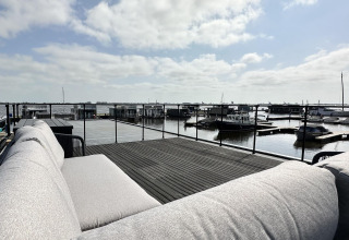 Vista desde una terraza en el Houseboat 'Riggelbrug' con sofá, agua y barcos en Friesland, Países Bajos.