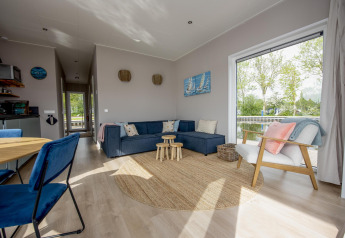 Soggiorno moderno nella houseboat 'Riggelbrug' con grande finestra, divano blu e vista sul canale in Friesland.