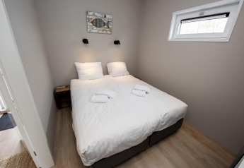 Cozy bedroom with double bed, white linens, bedside tables and wall art at Houseboat 'Riggelbrug', Friesland.
