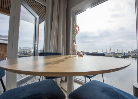 Área de comedor luminosa en Houseboat 'Riggelbrug', Friesland, Países Bajos, con vistas al puerto exterior.