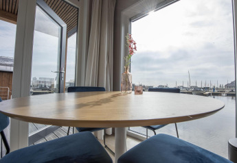 Zona pranzo luminosa su Houseboat 'Riggelbrug', Friesland, Paesi Bassi, con vista sul porto dalla finestra.