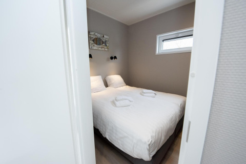 Dormitorio moderno con cama doble, sábanas blancas y toallas en Houseboat 'Riggelbrug', Friesland, Países Bajos.
