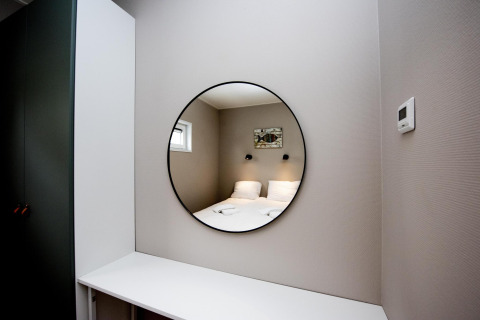 Modernes Zimmer im Houseboat 'Riggelbrug' in Friesland mit rundem Spiegel, der ein Bett widerspiegelt.