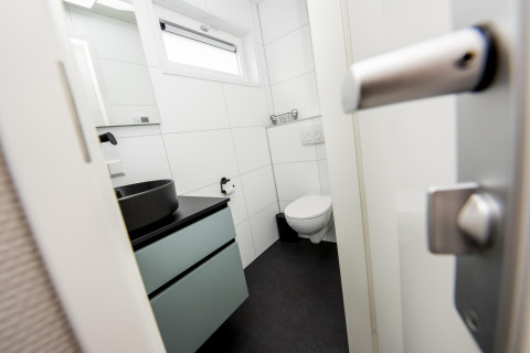 Baño moderno con inodoro suspendido, lavabo negro y ventana en Houseboat 'Riggelbrug' en Friesland, Países Bajos.