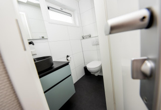 Baño moderno con inodoro suspendido, lavabo negro y ventana en Houseboat 'Riggelbrug' en Friesland, Países Bajos.