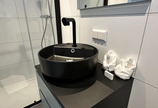 Moderne badkamer met zwart ronde wasbak, stijlvolle kraan en opgevouwen handdoeken op zwart blad.