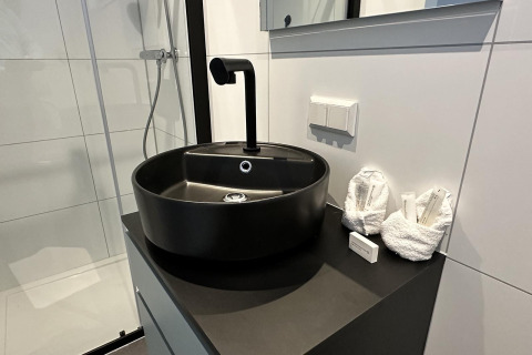 Baño moderno con lavabo negro redondo, grifo elegante y toallas plegadas sobre encimera oscura en la casa flotante.