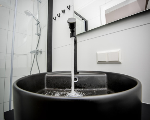 Moderno lavabo negro con agua corriendo en el baño de la casa flotante 'Riggelbrug', Welcome In - Friesland, Países Bajos.