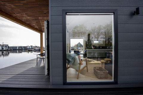 Vista de la casa flotante Riggelbrug en Welcome In - Friesland, Países Bajos, con interior moderno y terraza junto al agua.