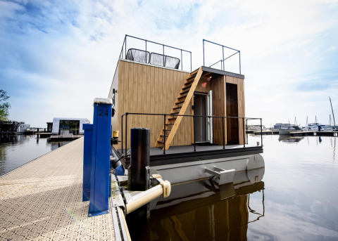 Moderno Houseboat 'Riggelbrug' en Welcome In - Friesland, Países Bajos, atracado junto a un muelle tranquilo.
